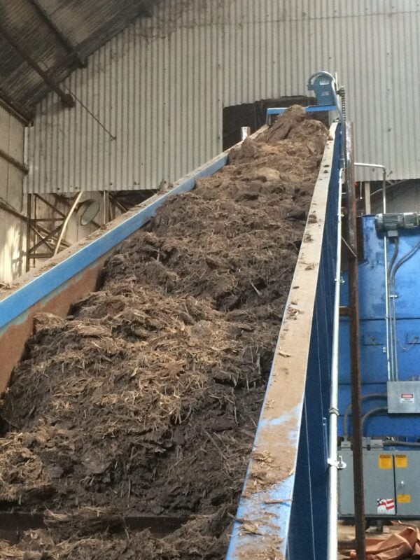 A conveyor belt filled with dirt and wood chips.