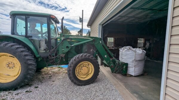 A green tractor parked in front of a garage.