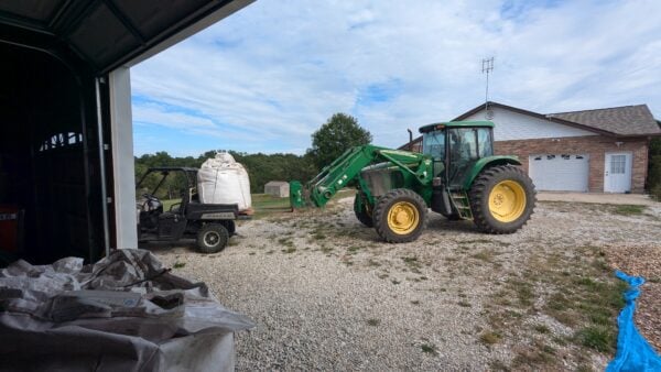 A tractor is parked in the gravel near a trailer.